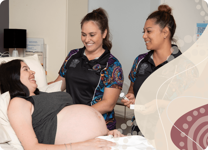 A smiling pregnant women about to receive a scan looking up at two health workers